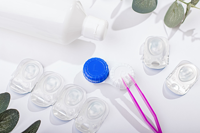 Contact lens kit with lenses, bottle of lens solution, case and tweezers on a white table.