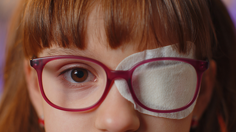 Close up of girl’s face having a protective bandage plaster patch on one eye.
