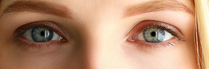 The image is a close-up of a person's eyes. The eyes are open, revealing striking blue irises with a clear, detailed reflection in the pupils.